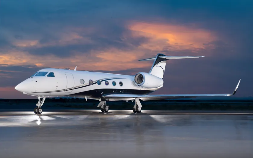 Jet privado Gulfstream G450 aparcado en la plataforma al anochecer, bajo un espectacular cielo de puesta de sol