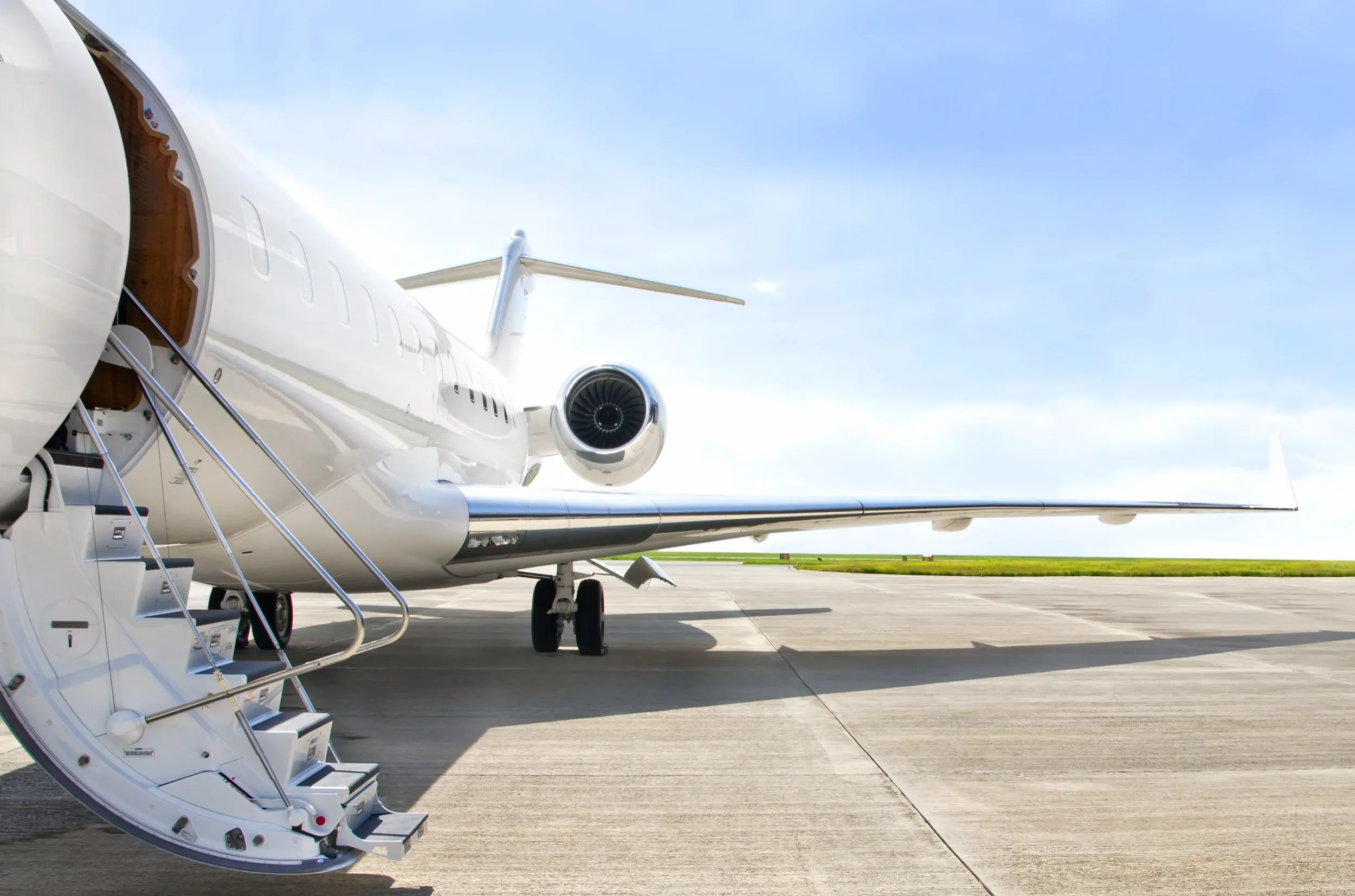 Un jet privado en la pista, con la escalerilla desplegada bajo un cielo azul despejado.