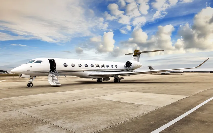 Jet privado Gulfstream G700 blanco con filetes dorados aparcado en una plataforma, con la escalerilla desplegada