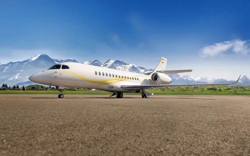 Jet privado Dassault Falcon 6X aparcado en la plataforma con montañas nevadas al fondo