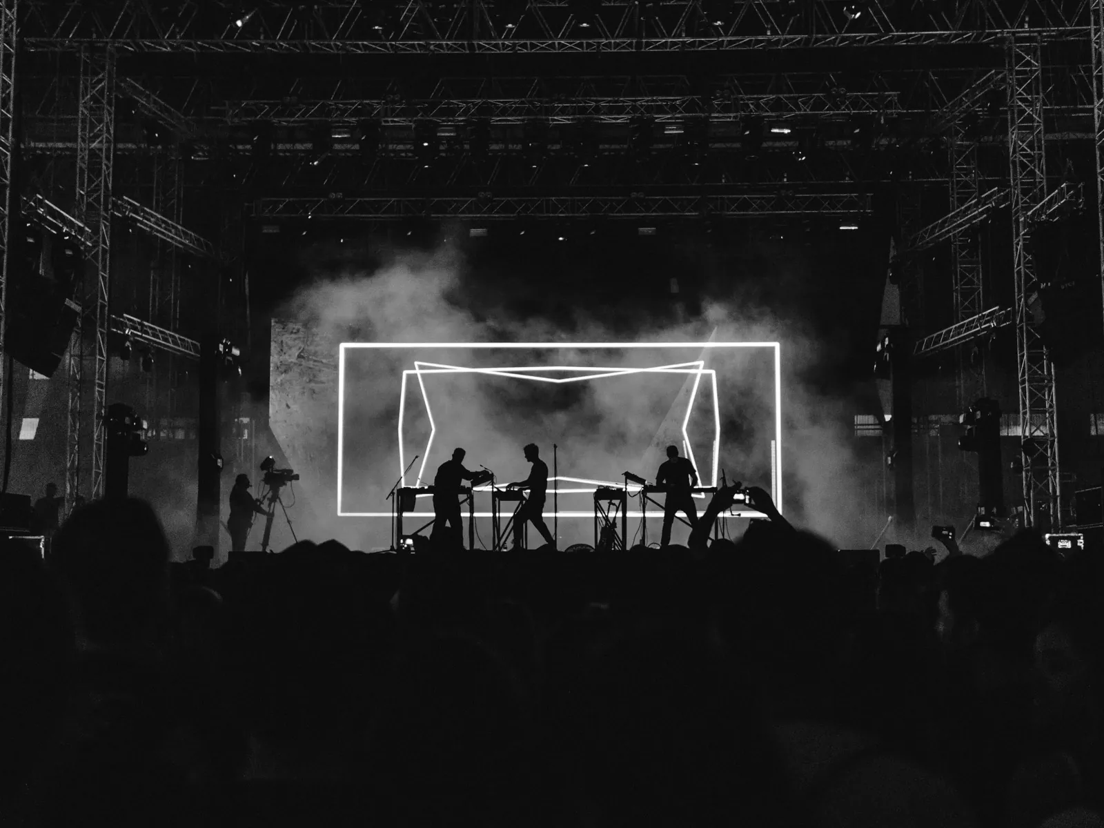 Siluetas de artistas sobre un escenario de concierto envuelto en humo e iluminado por focos intensos