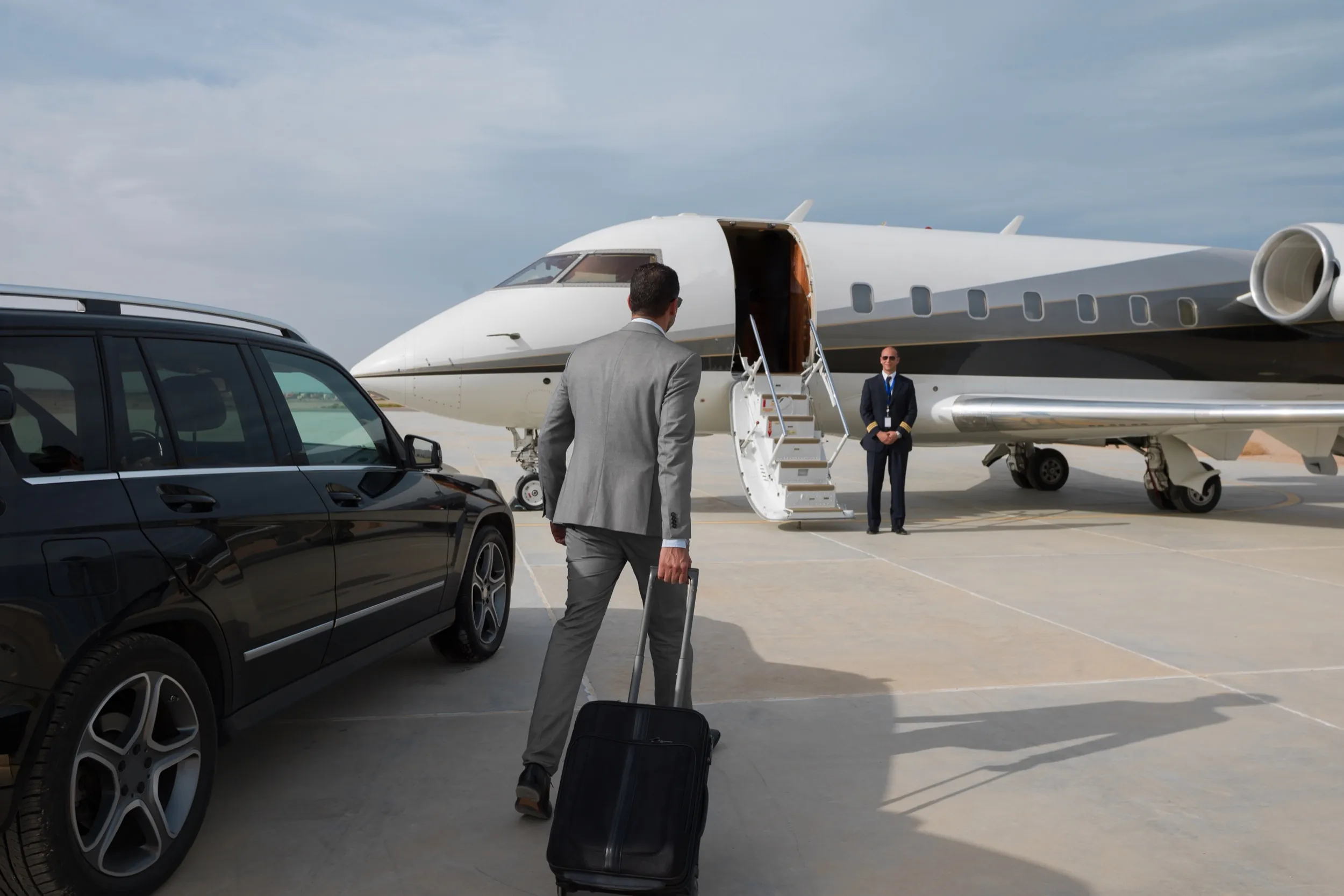 Un viajero de negocios camina desde un coche con chófer hacia un jet privado mientras la tripulación espera