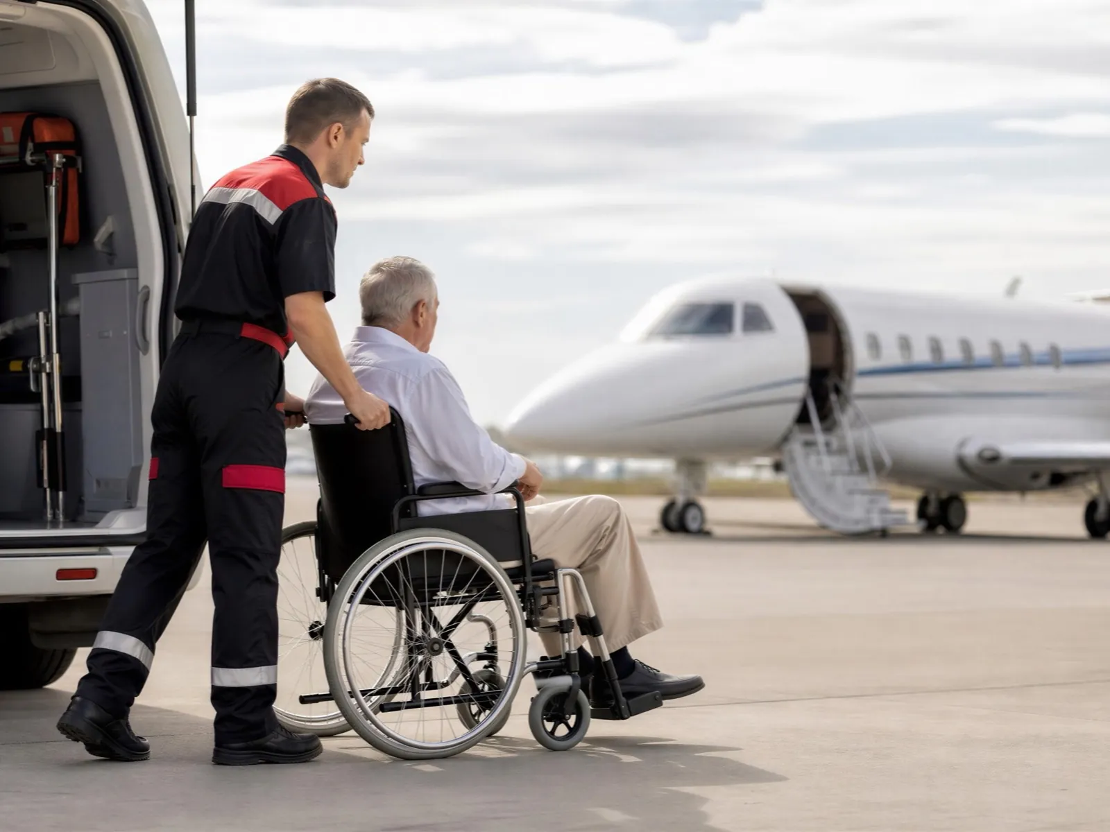 Un sanitario traslada a un paciente en silla de ruedas hacia un jet privado junto a una ambulancia