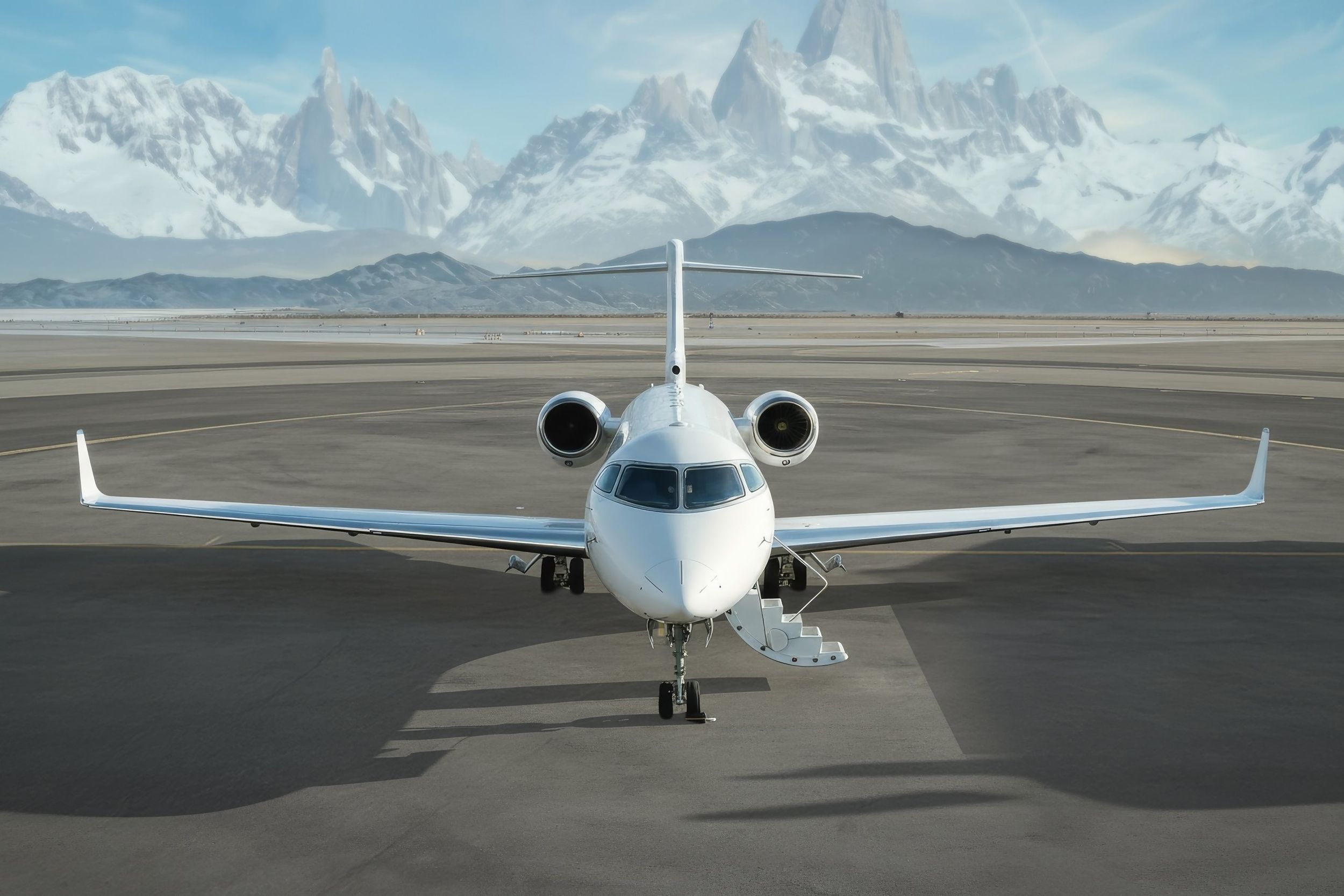 Private jet on a runway with snow-capped mountains behind it