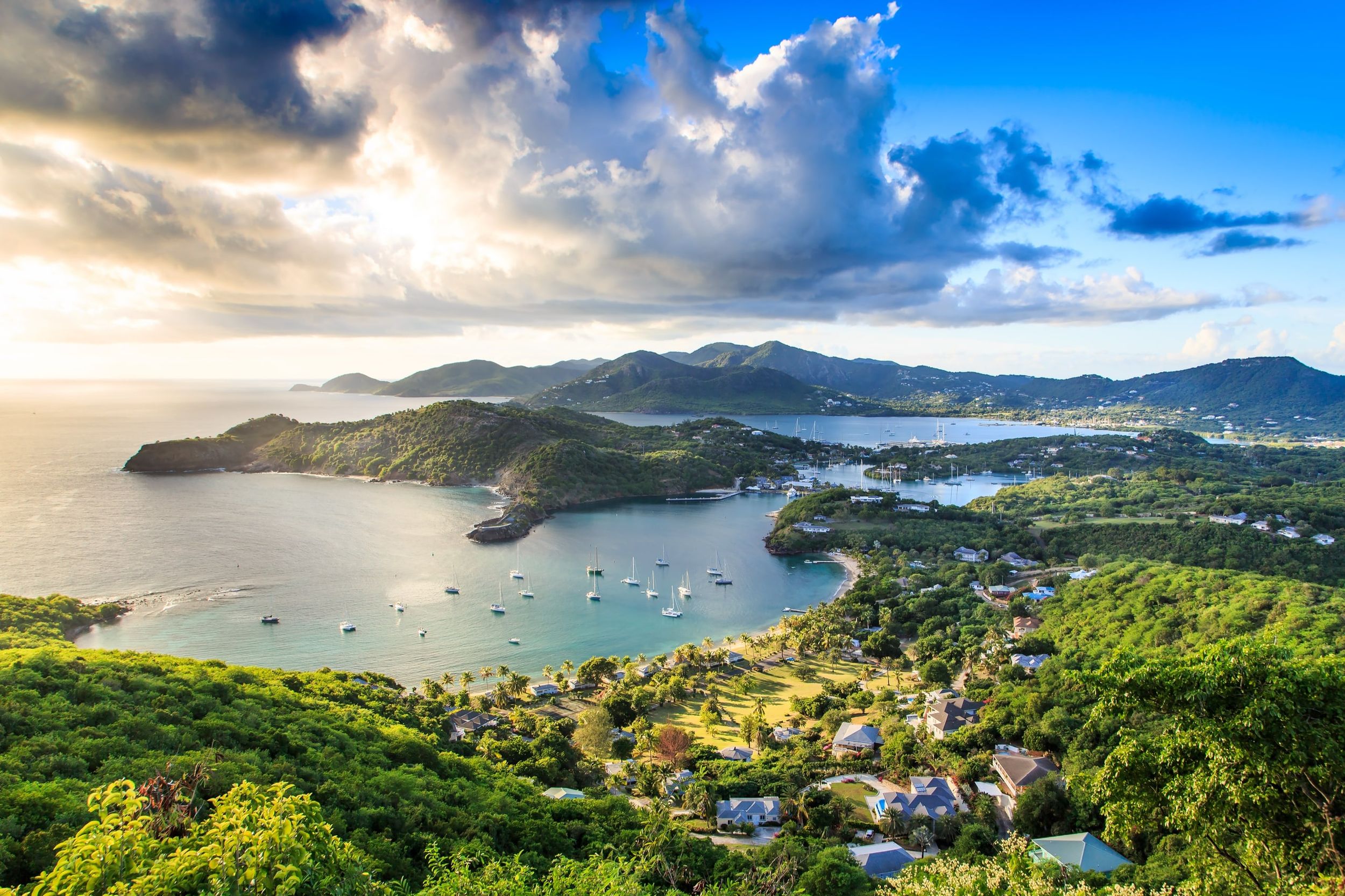 Aerial view of a Caribbean harbour at sunset, with yachts moored in a turquoise bay below green hills