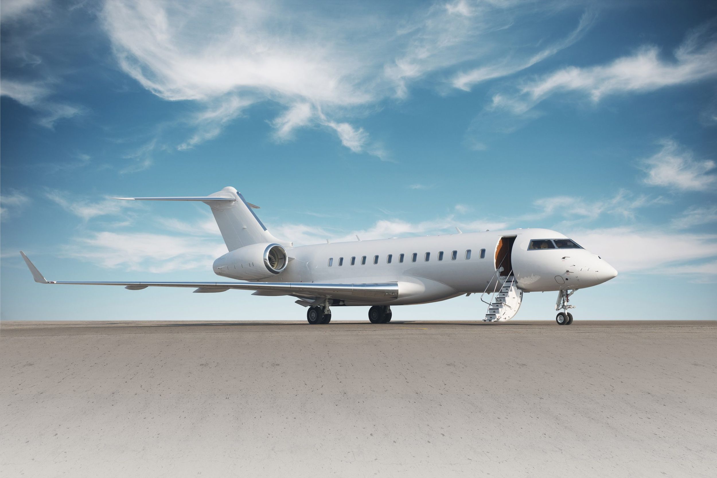 Un jet privé Bombardier Global, passerelle déployée, sur l'aire de stationnement sous un ciel bleu