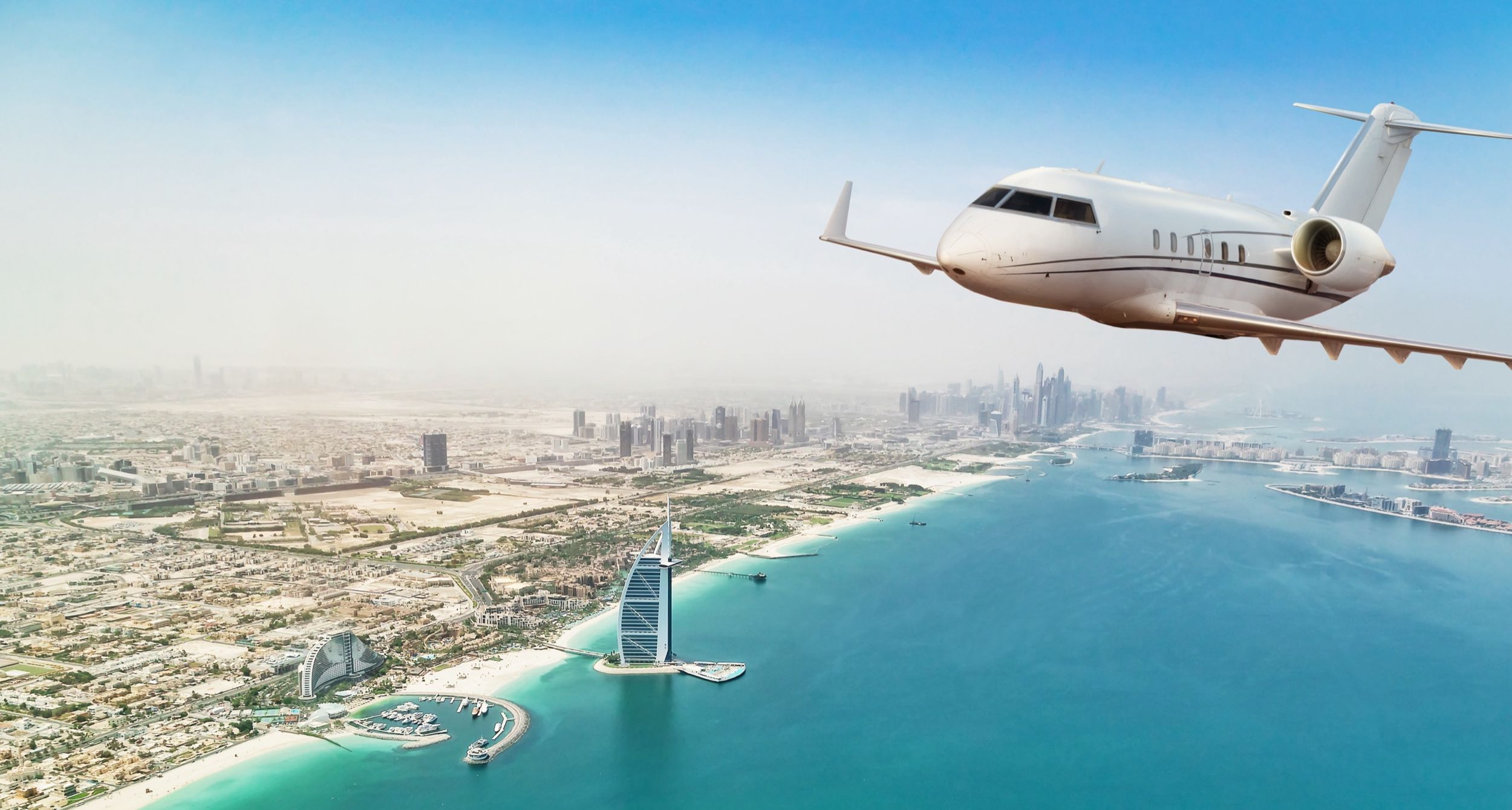 A private jet in flight above the Dubai coastline and the Burj Al Arab