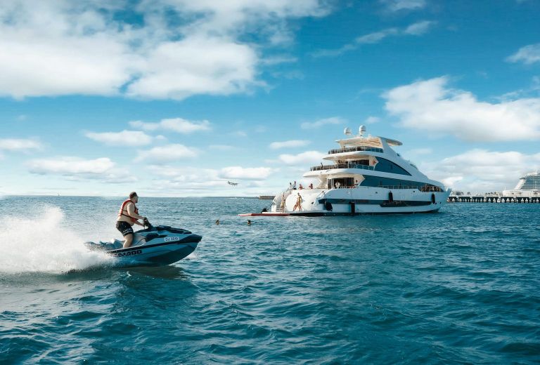 A jet ski speeds past a luxury yacht moored in turquoise water