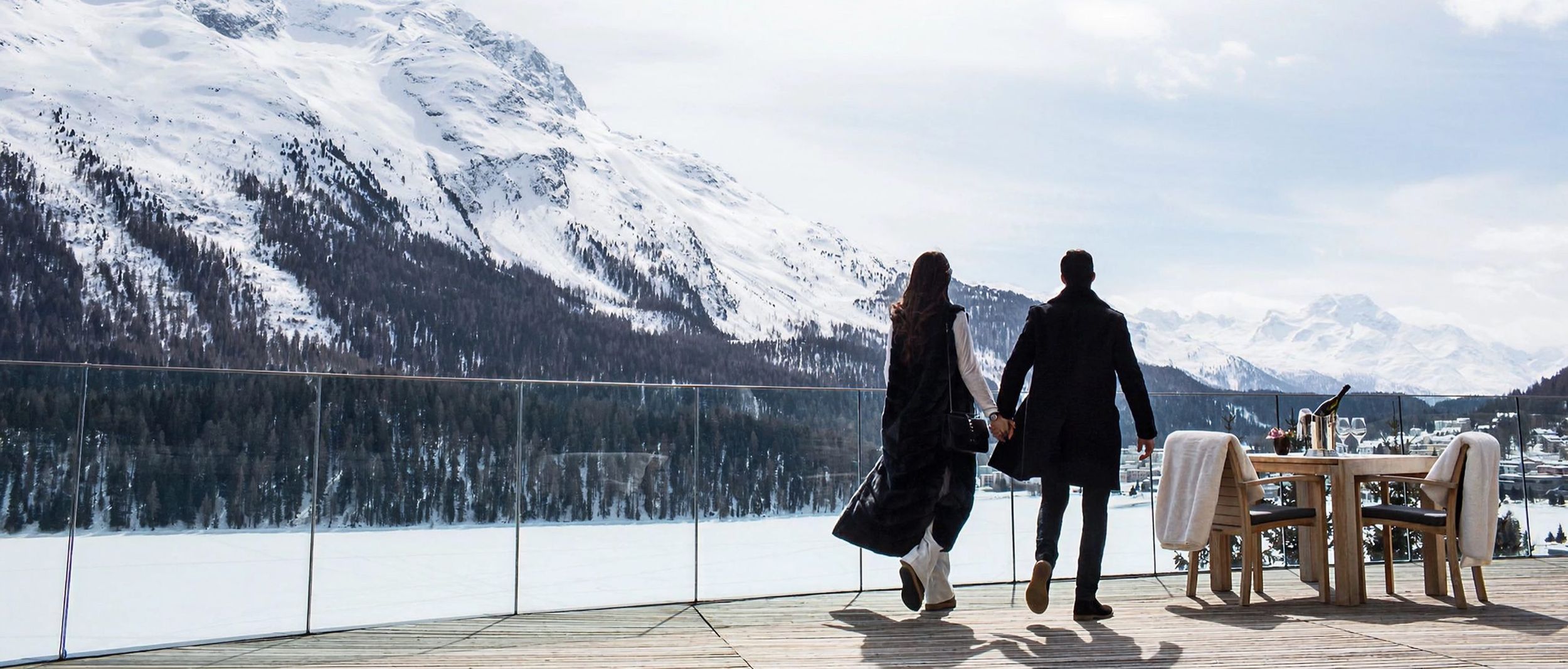 A couple walking hand in hand on a terrace overlooking snow-capped mountains