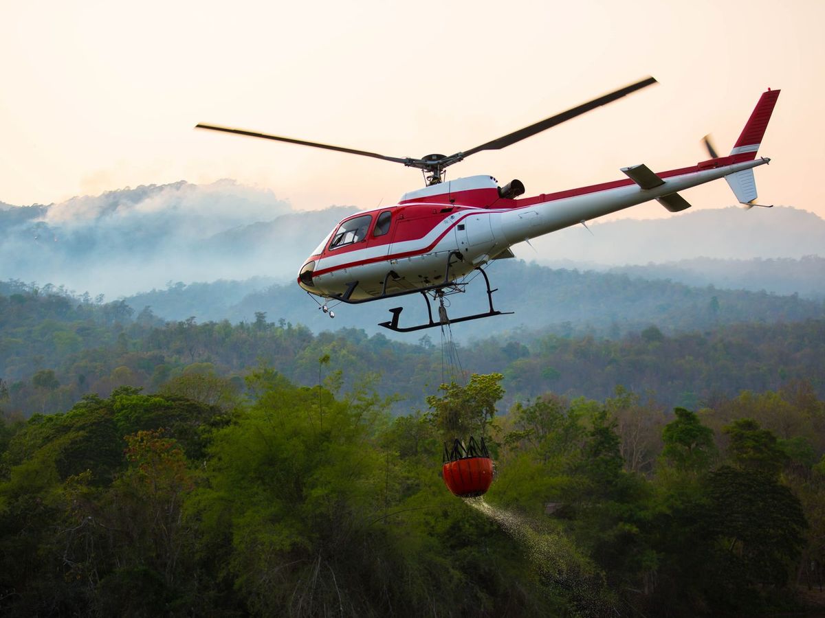 A rescue helicopter carrying a load over forested terrain