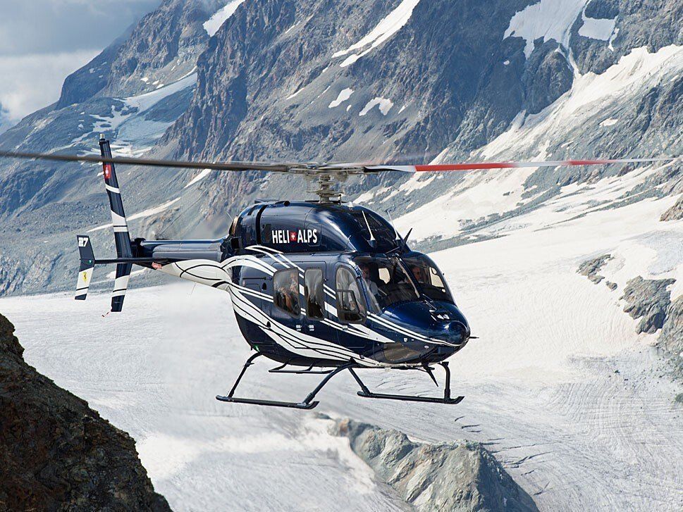 A twin-engine helicopter in flight over snow-covered mountains