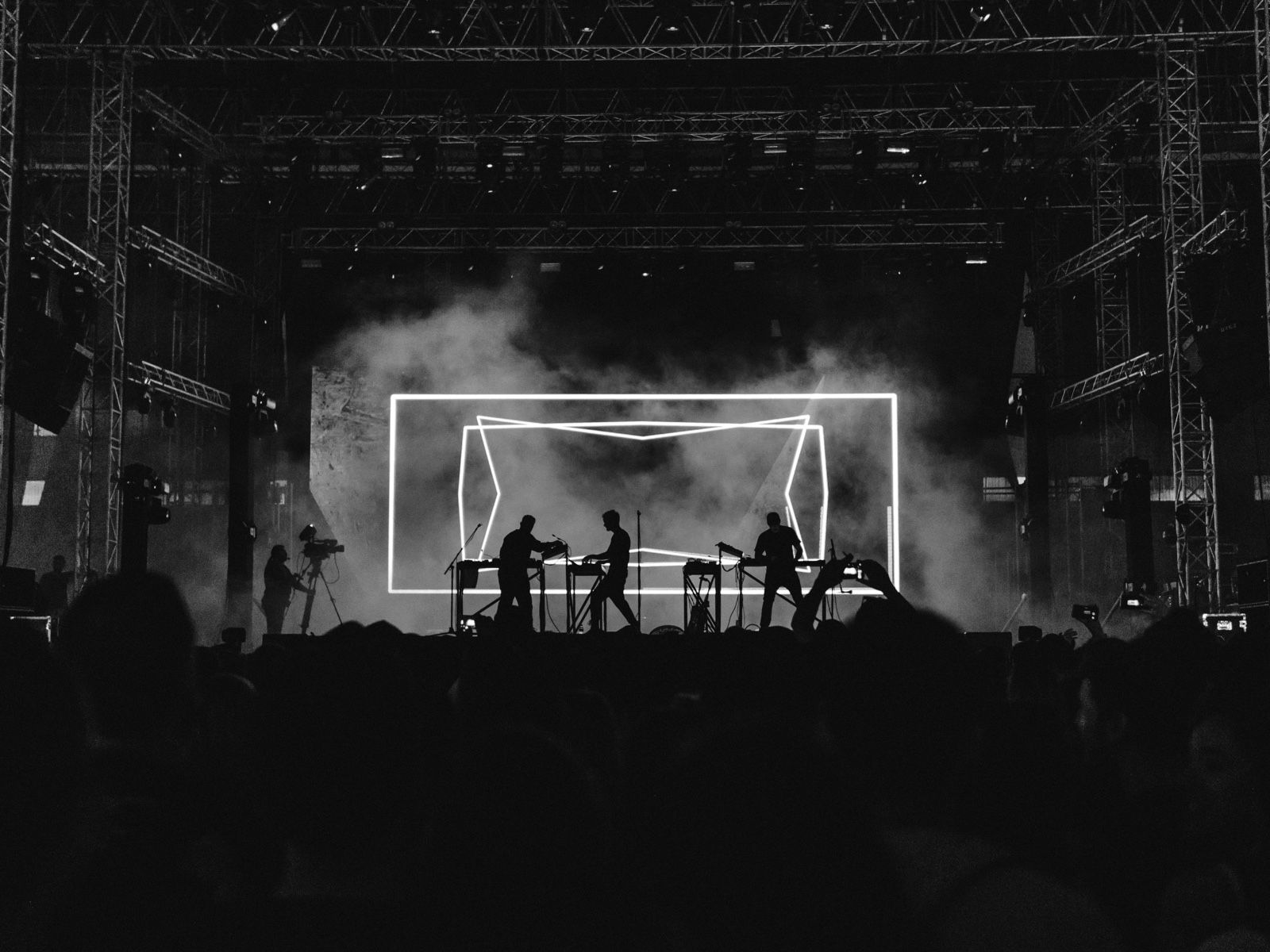Silhouetted performers on a smoke-filled concert stage lit by bright lights