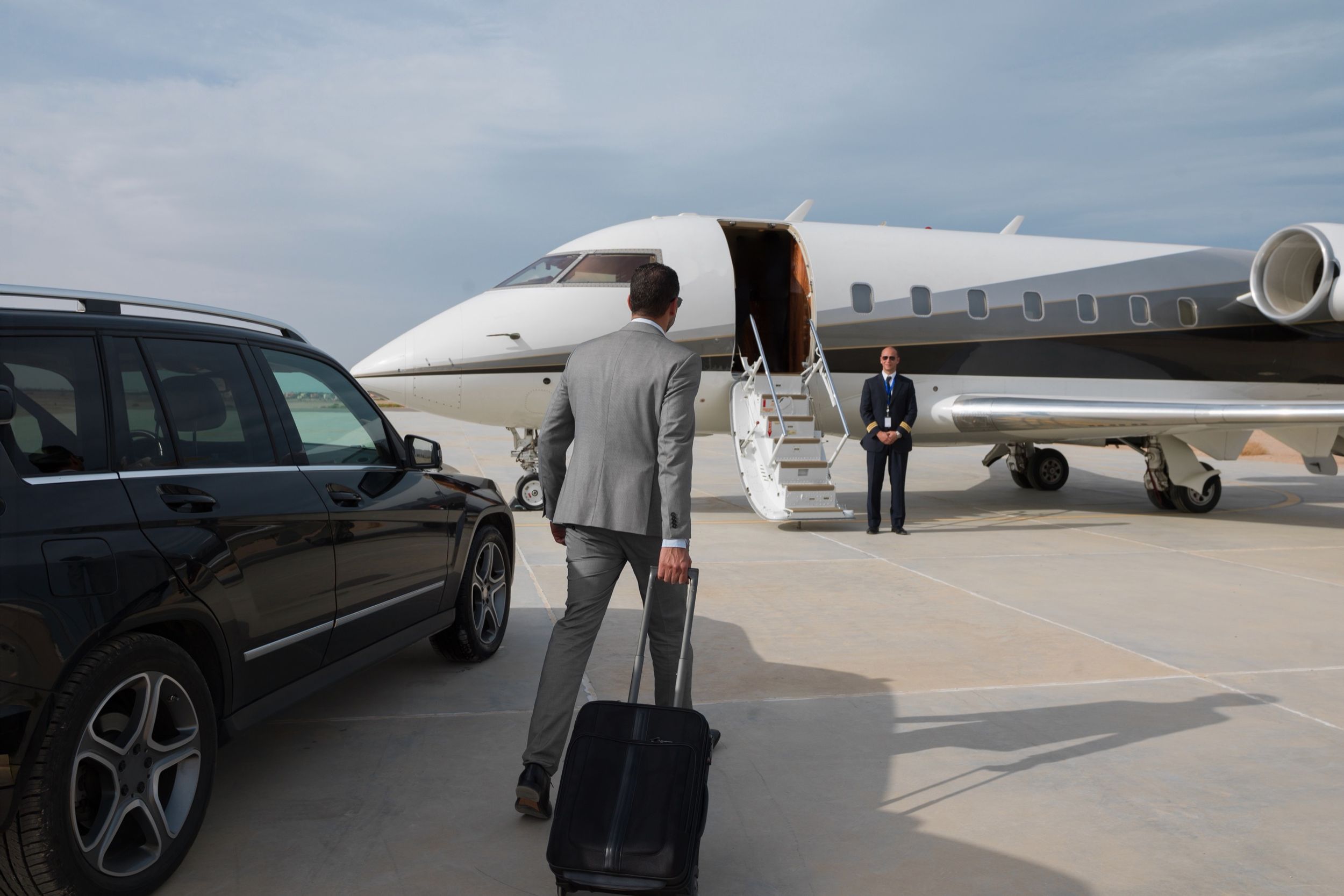 A business traveller walking from a chauffeured car to a private jet as the crew waits